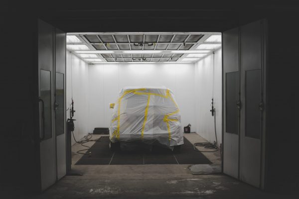 A vehicle covered with a white sheet and yellow tape in a car service garage